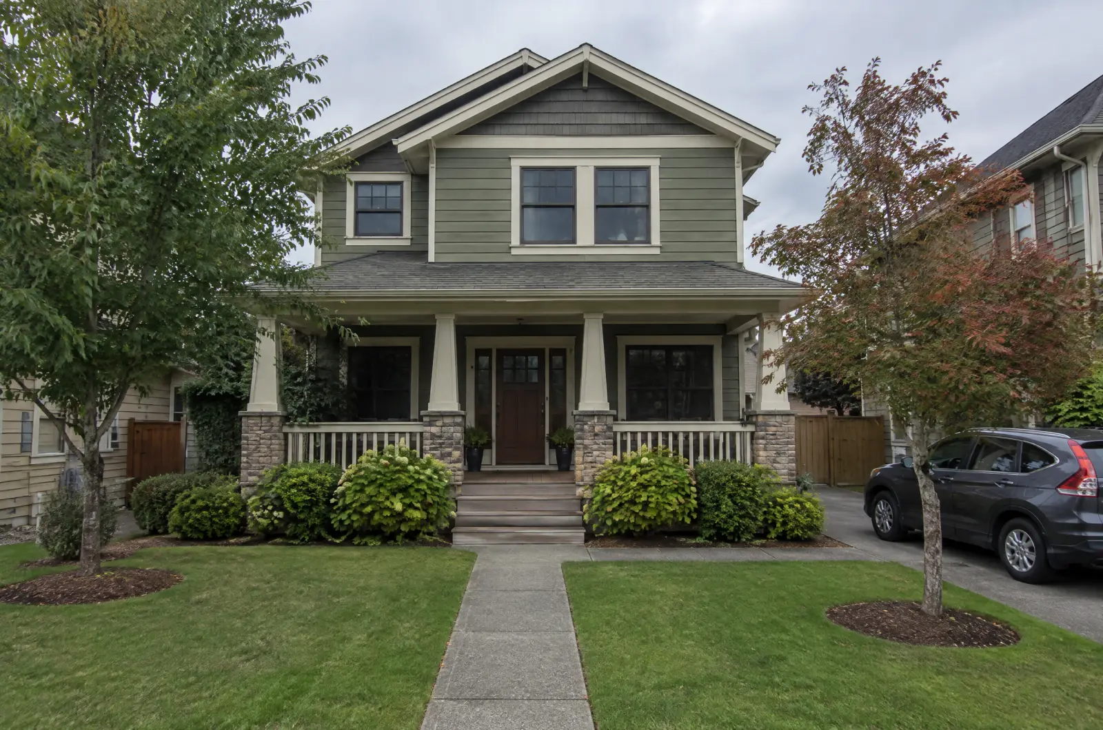 A two-storey house with a porch under a grey midday sky, lights off.